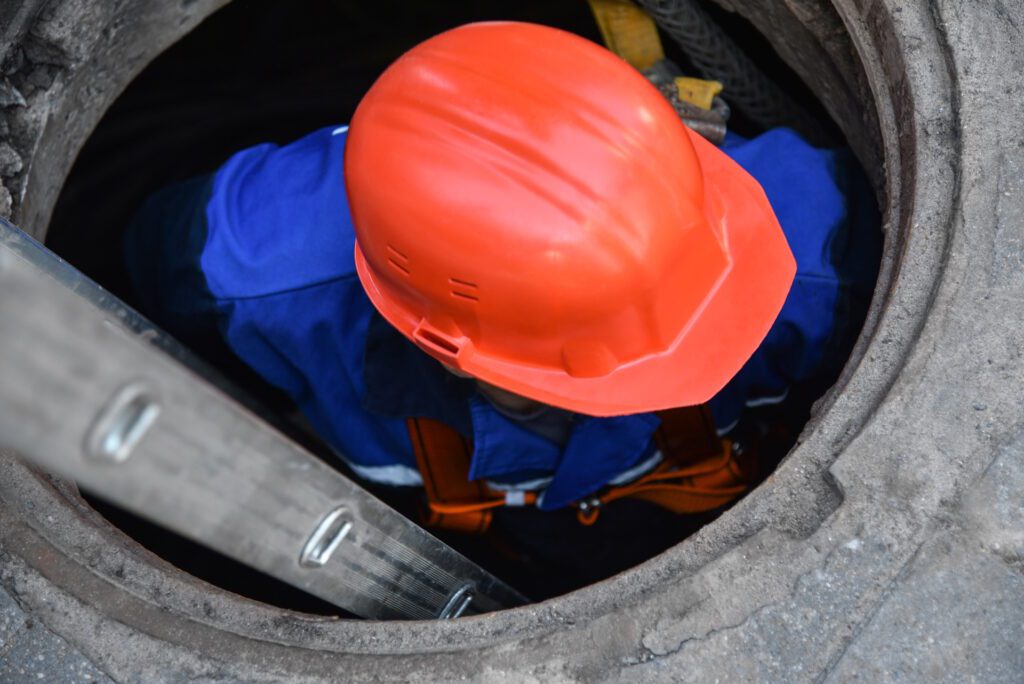 Worker In A Helmet Descends Into A Cable Well